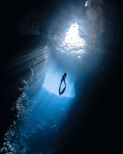 Buzo descendiendo entre rayos de luz en una cueva submarina